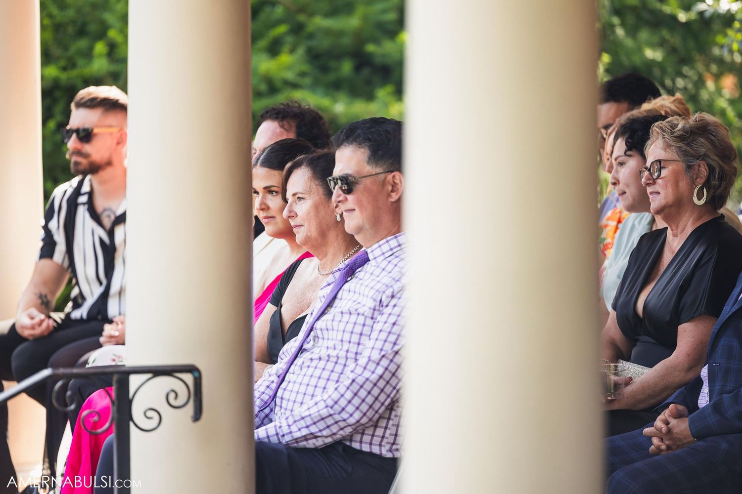 Wedding guests seated between elegant white columns at an outdoor ceremony venue.