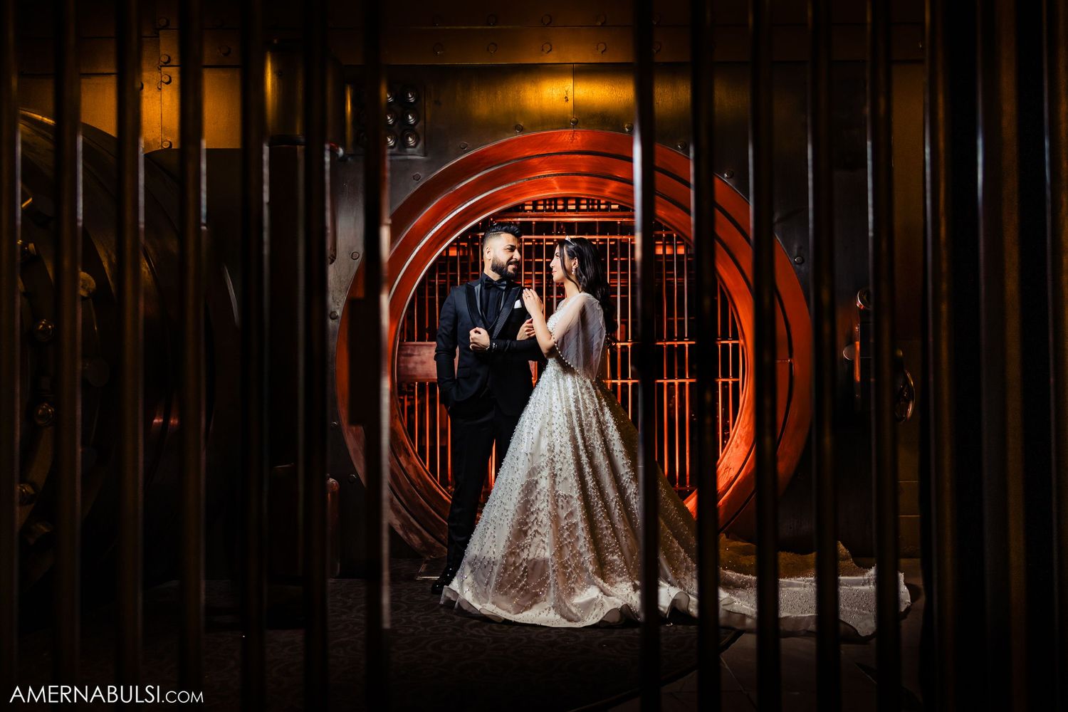 Dramatic wedding portrait in front of illuminated circular archway with warm red lighting and dark shadows.