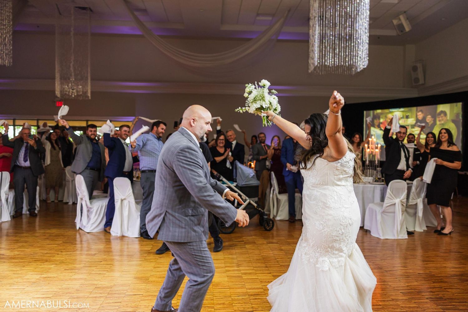 Dynamic dance moves during wedding reception with chandelier and ambient purple lighting.