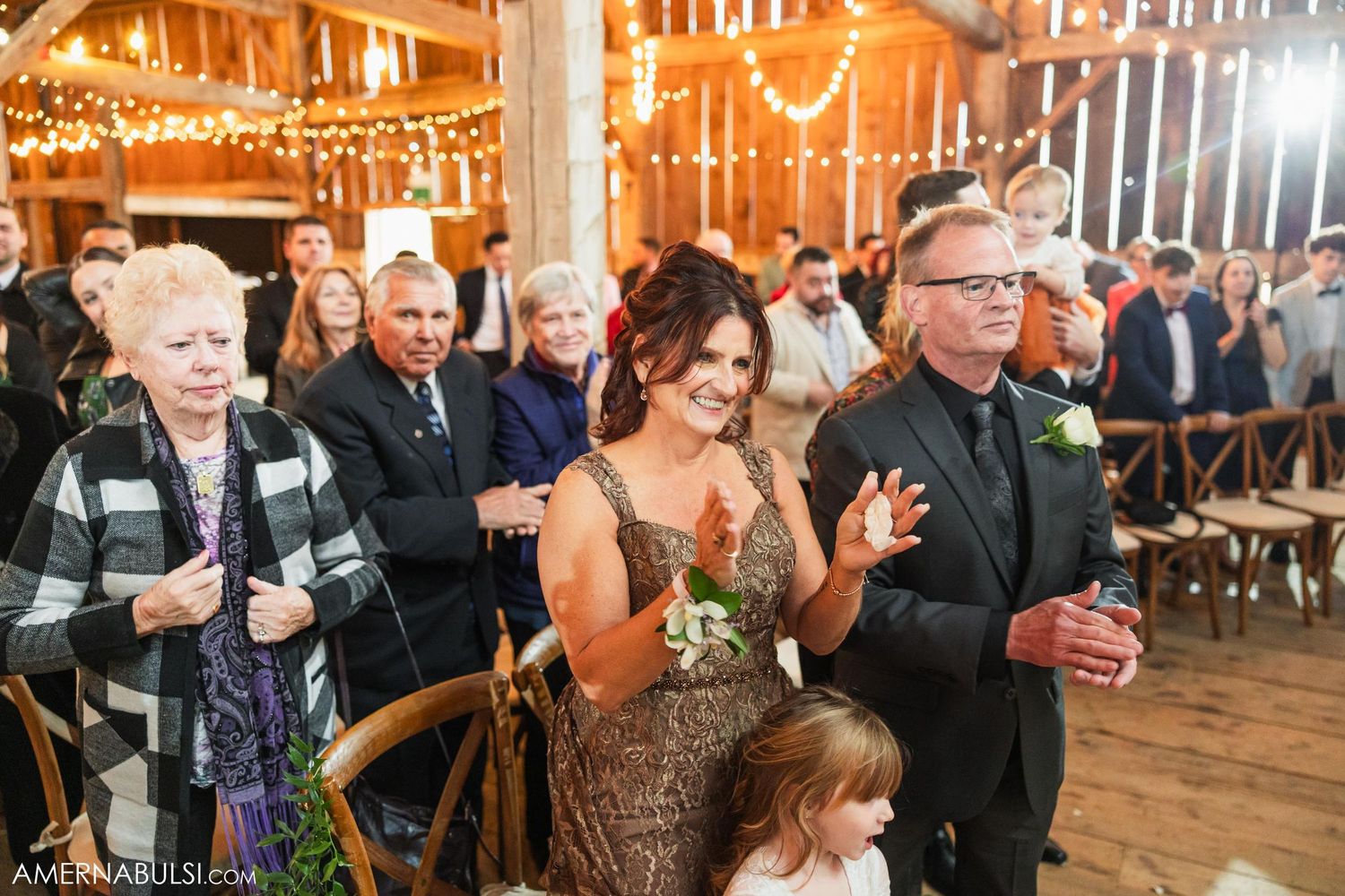 Wedding guests dance and celebrate in rustic barn reception with string lights.