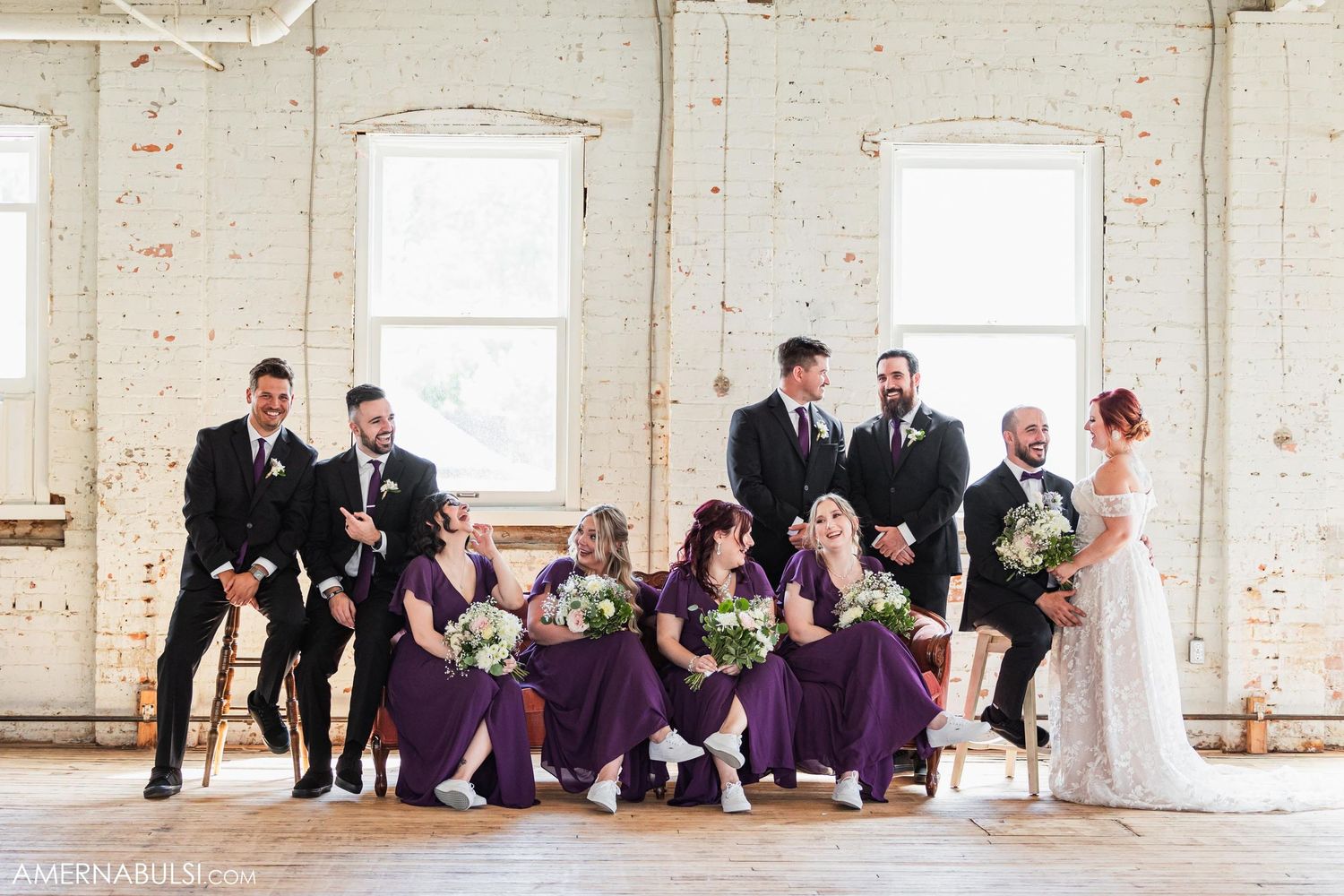 Fun wedding party photo with members sitting on window ledge in industrial space.