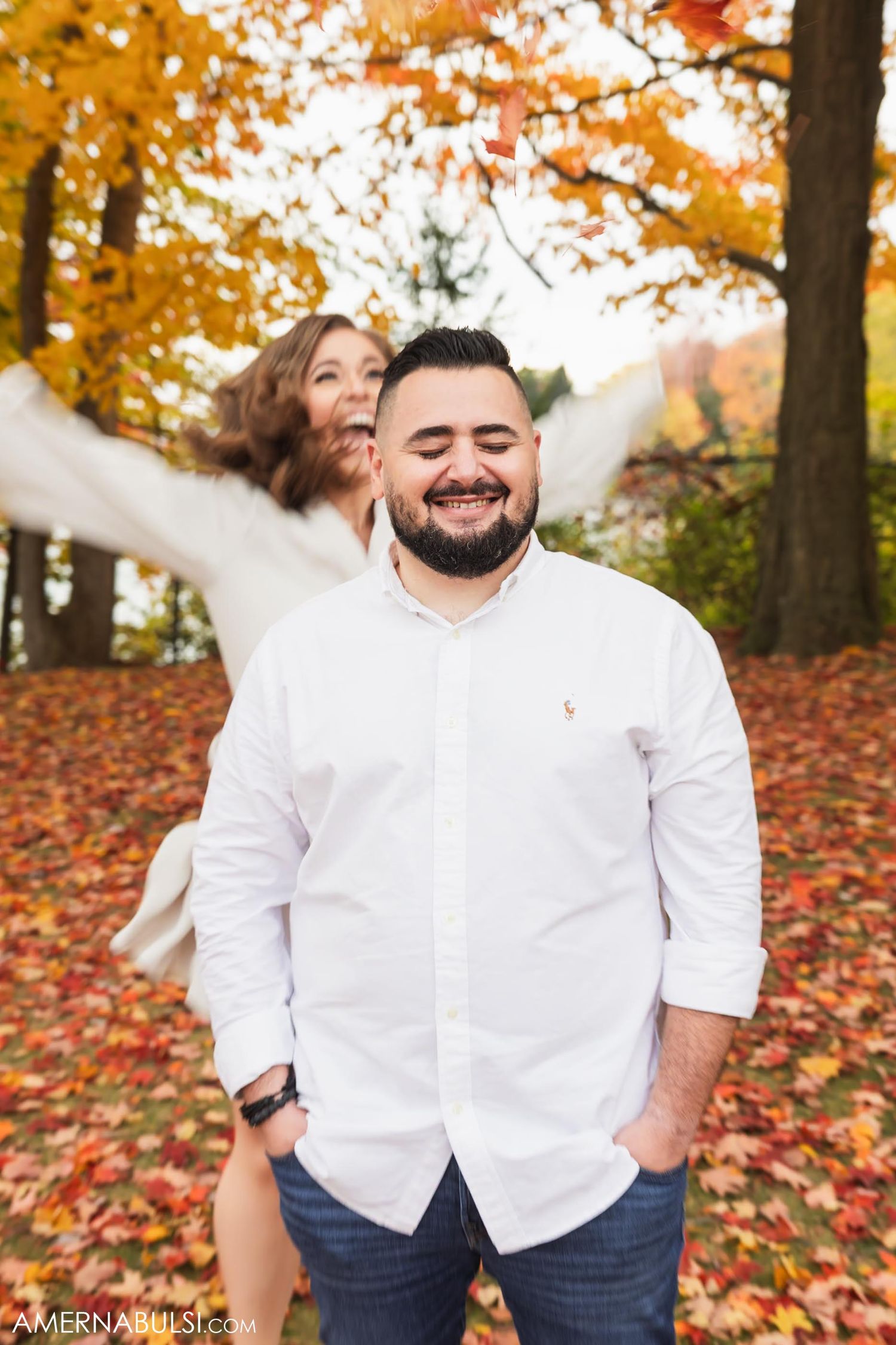 A playful fall engagement photo with leaves scattered on the ground.
