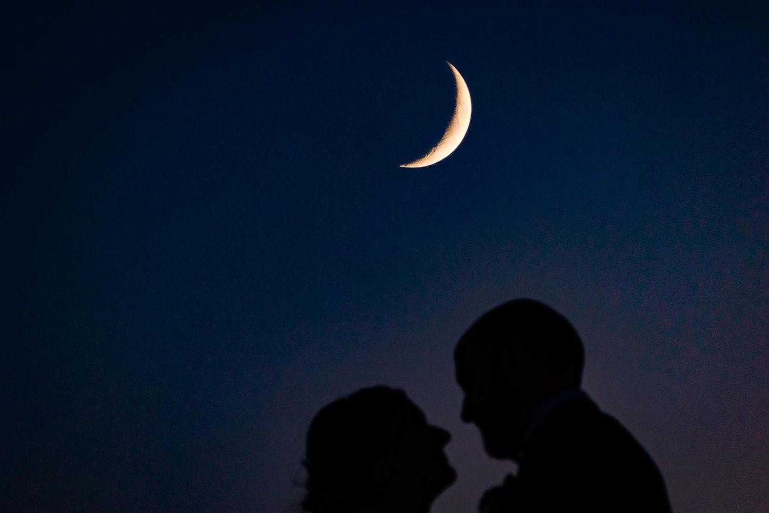 Silhouettes of two people against a dark night sky with a crescent moon.