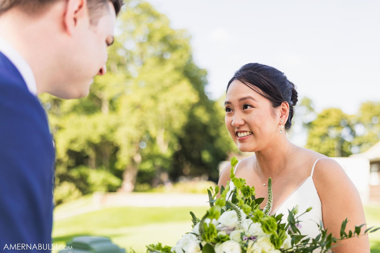 Candid moment between couple during outdoor wedding photoshoot with natural greenery background.