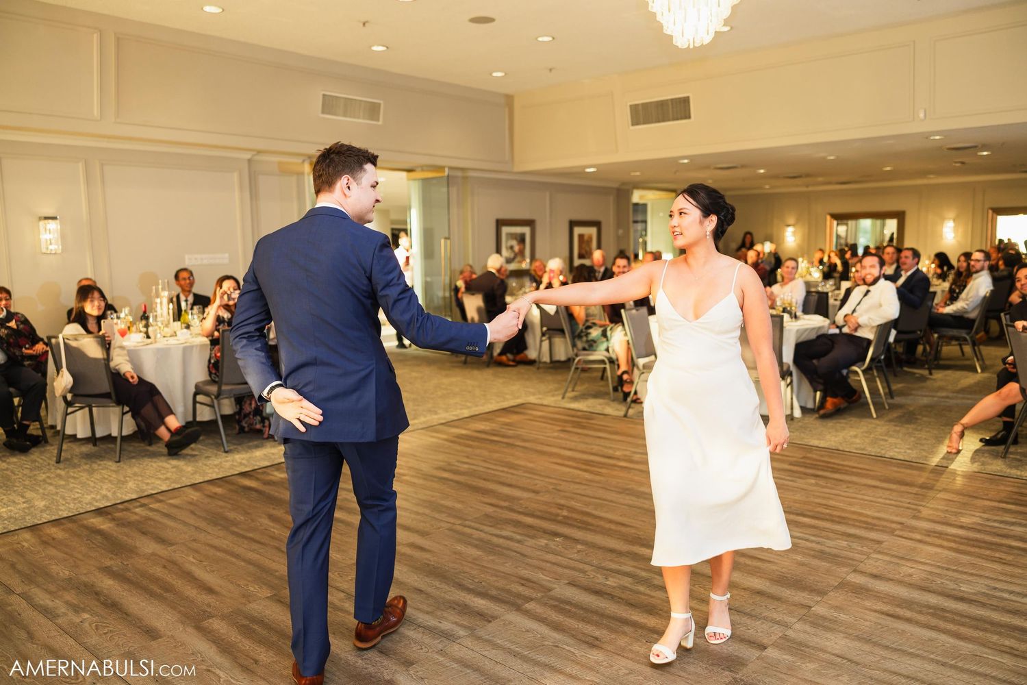 Wedding couple dances energetically on a wooden floor during their reception celebration.