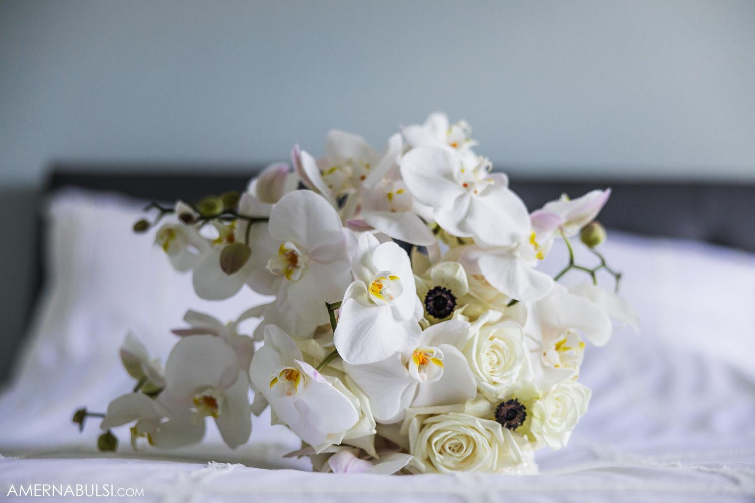 Elegant white orchid and rose bridal bouquet resting on white bedding.