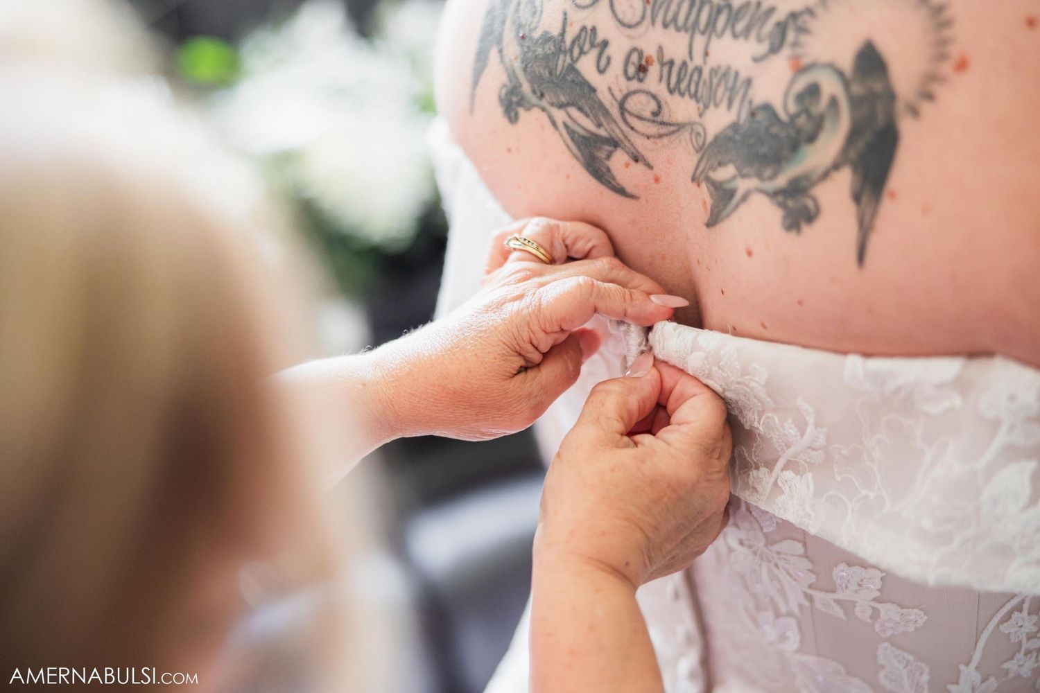 Close up of hands helping to fasten buttons on back of wedding dress.