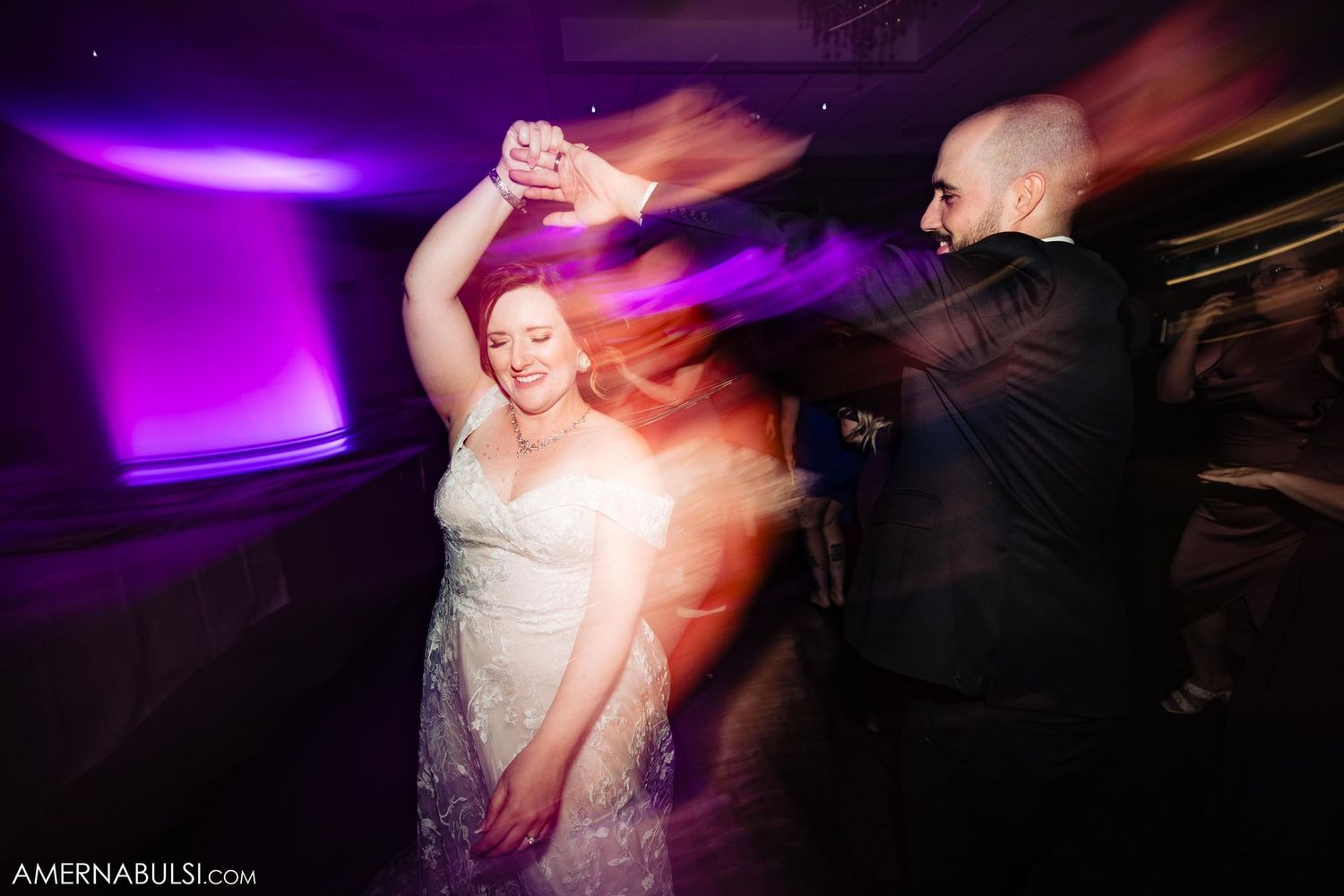 Wedding couple dancing under purple lights with motion blur effects.