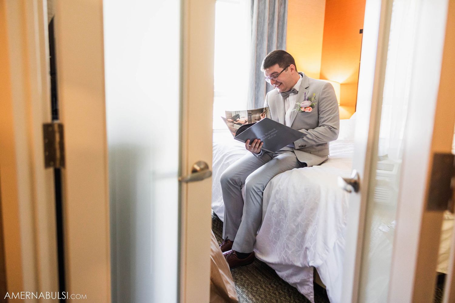 Person in formal gray attire sitting on bed reading papers in hotel room.