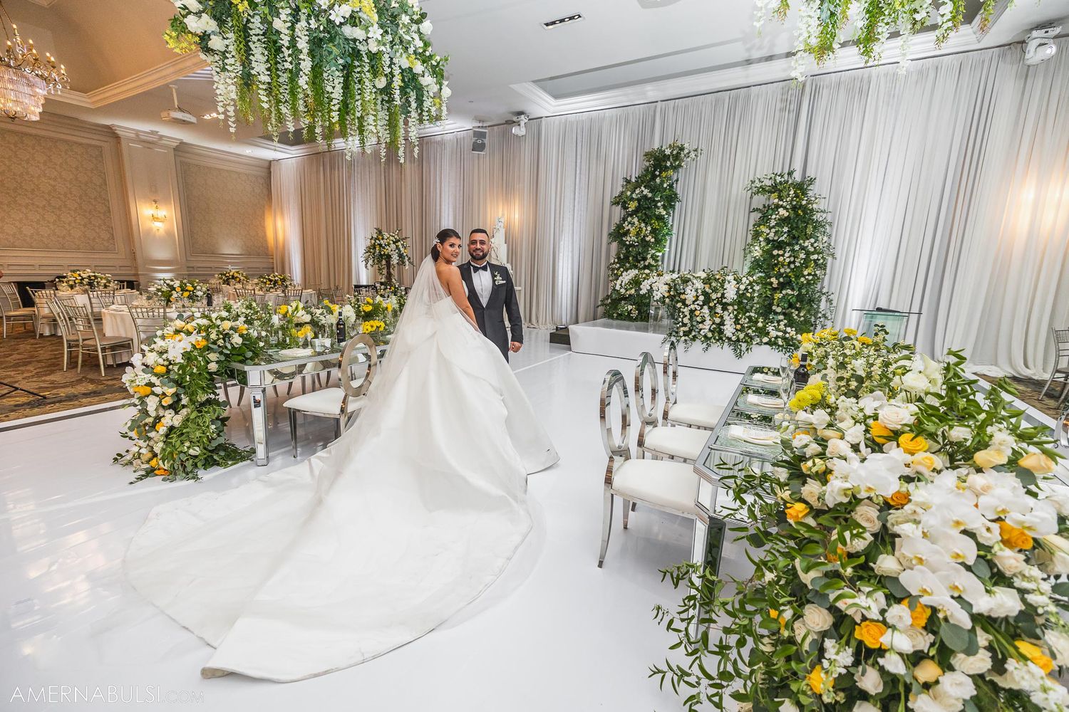 Wedding venue decorated with yellow and white floral arrangements and flowing white drapery.