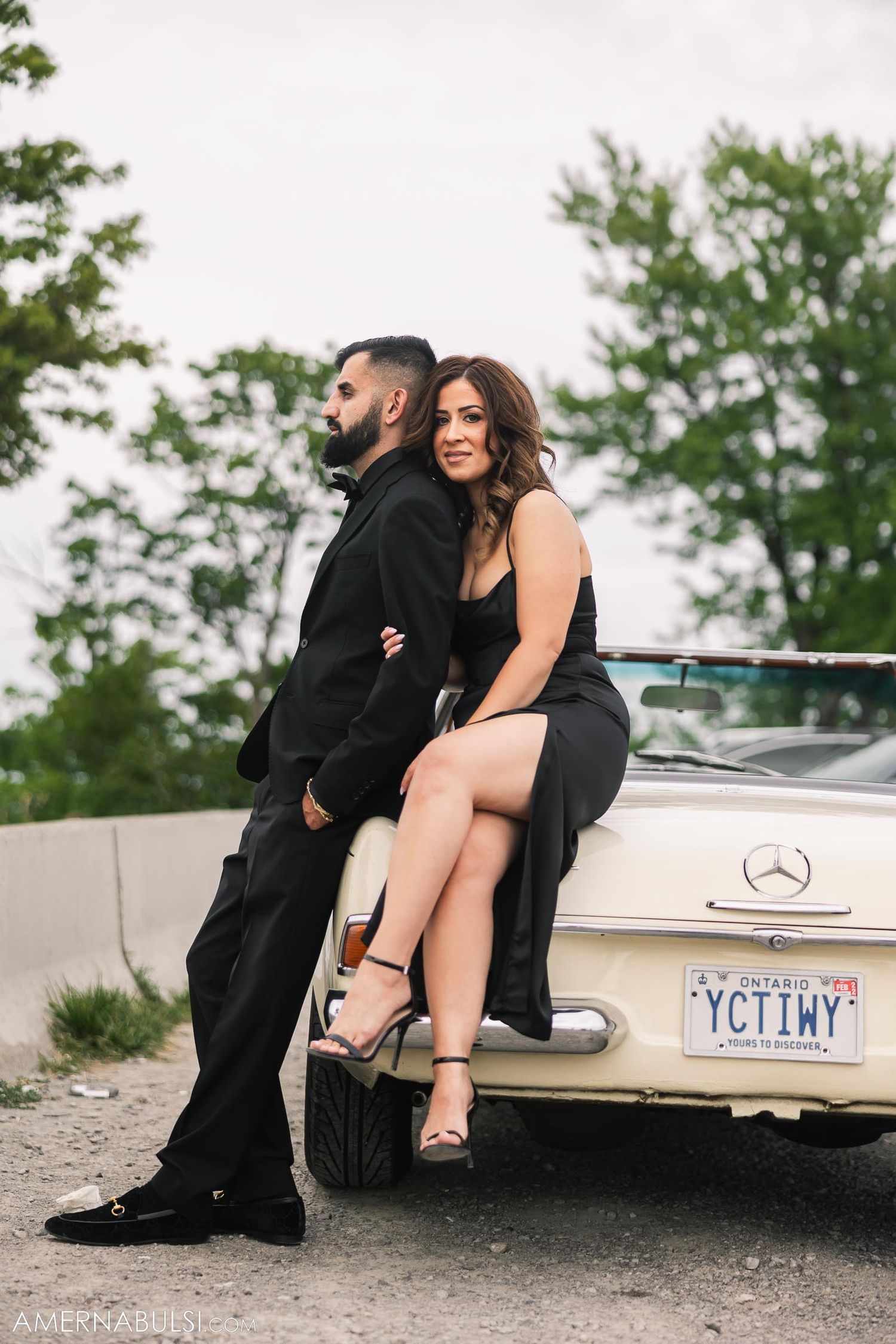 Stylish couple poses against a vintage Mercedes-Benz on an overcast day.