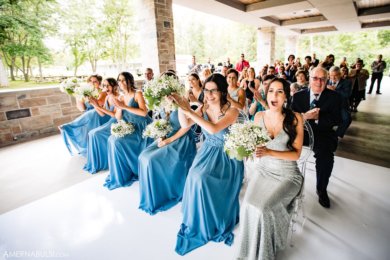 Wedding party members in blue dresses and formal attire dance together during a celebration at an outdoor venue.