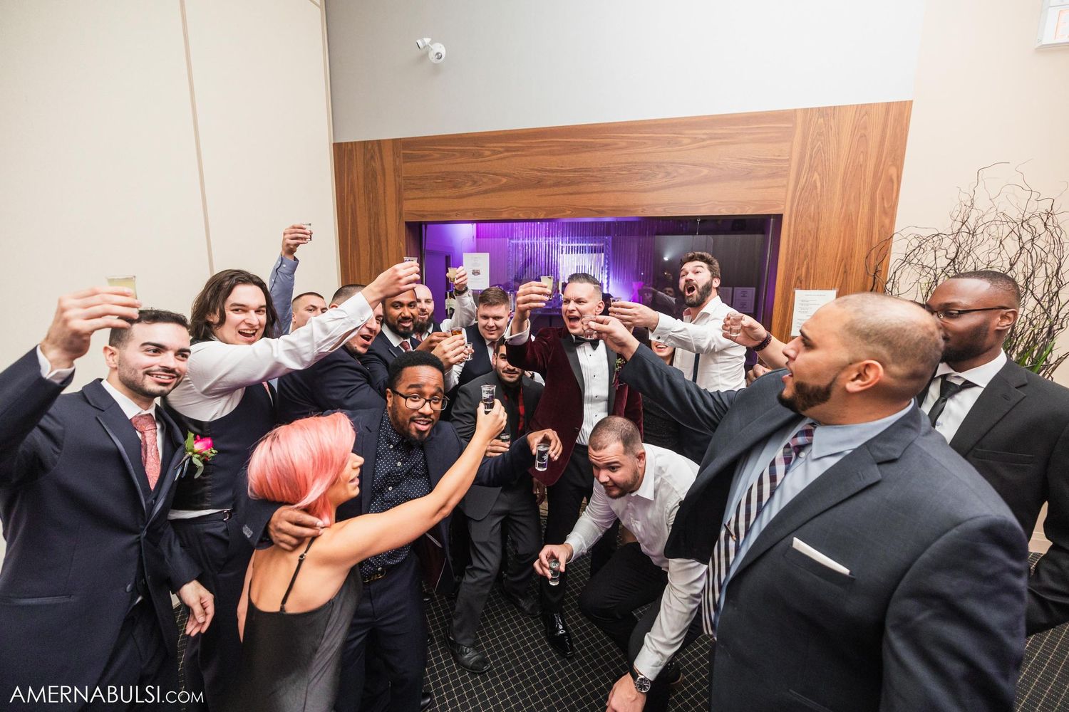 Wedding party members posing for fun group photo in hallway with energetic expressions.