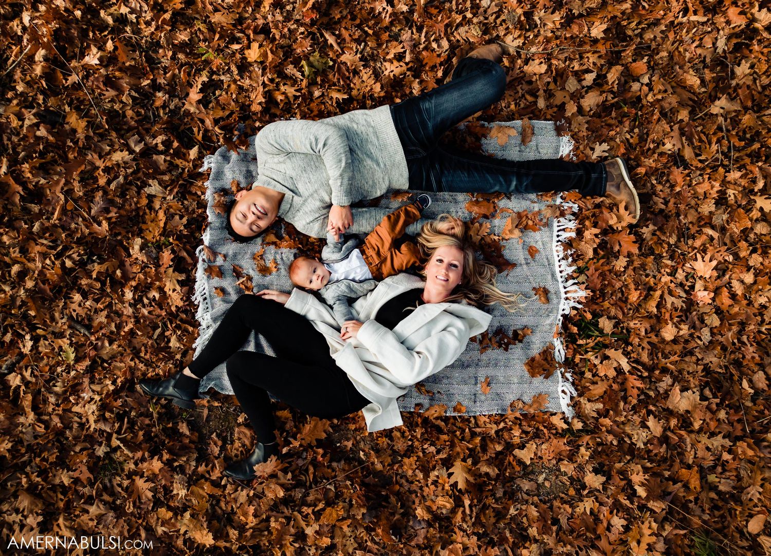 Birds-eye view of couple laying on grey blanket surrounded by brown fall foliage.