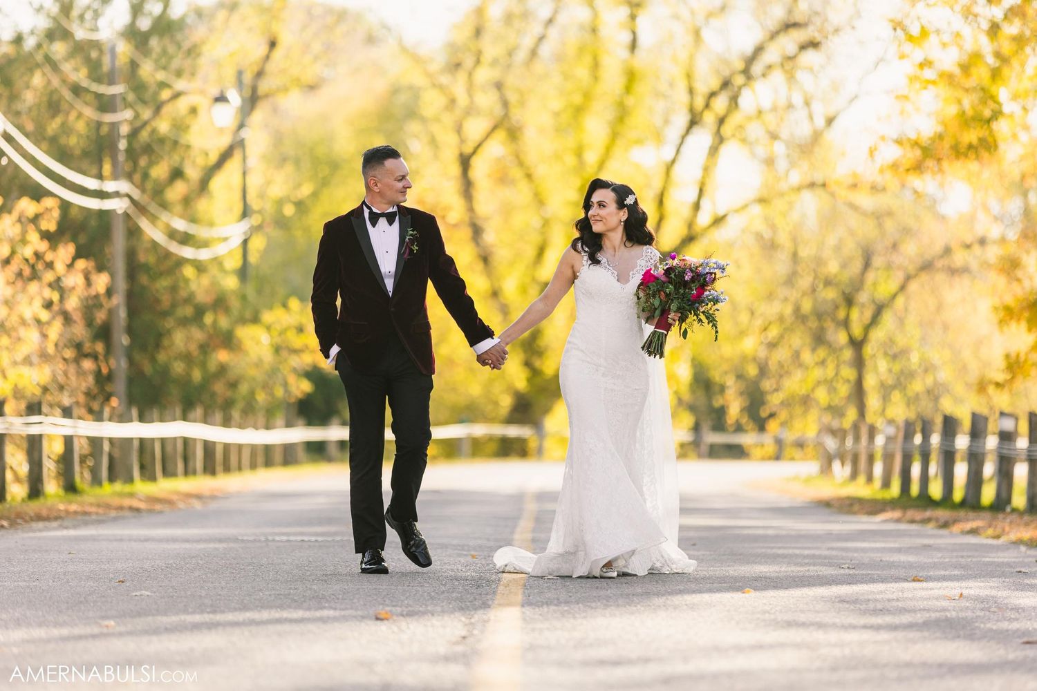 Couple walking hand in hand on tree-lined road during autumn.