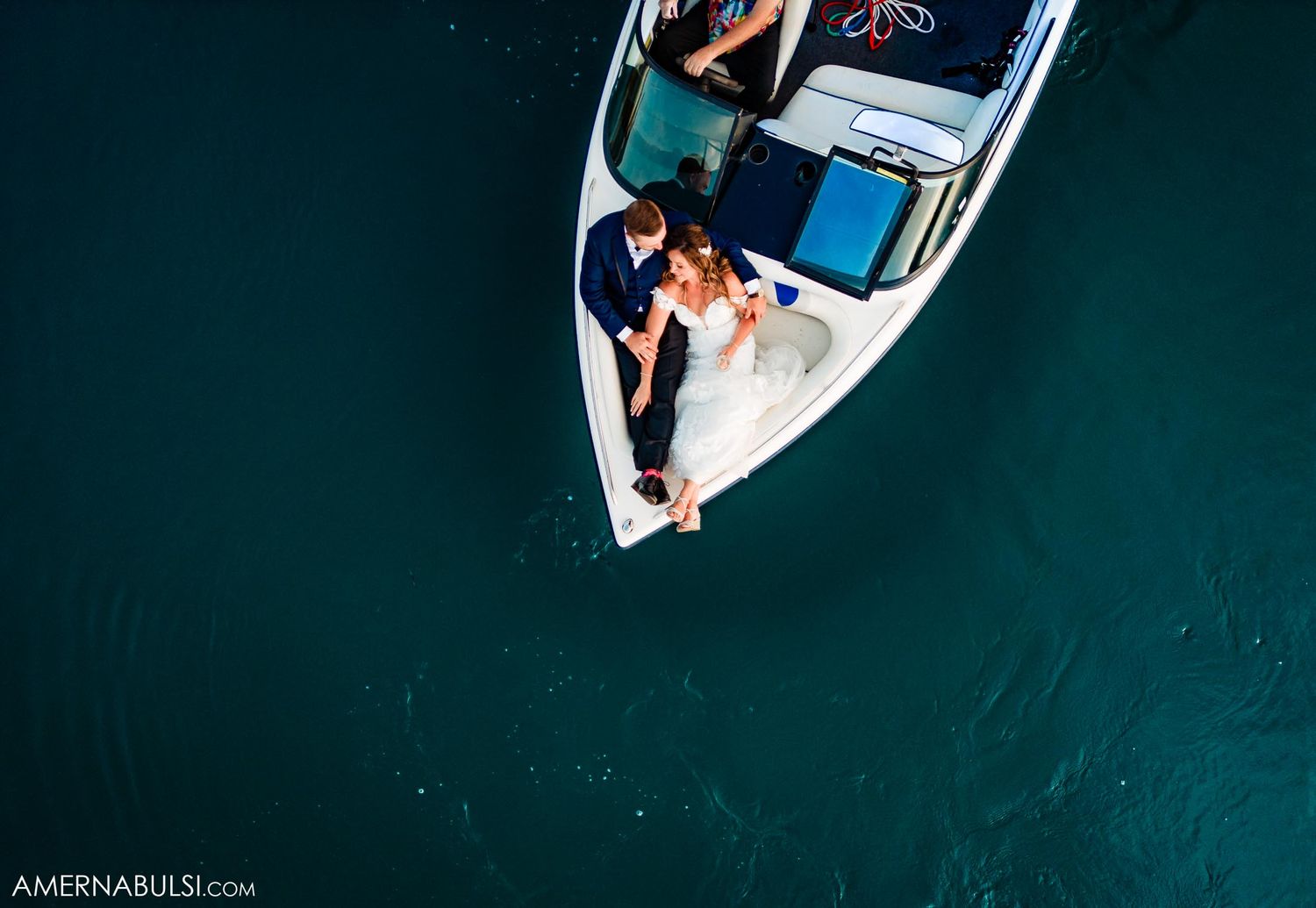 Aerial view of a couple lounging in a white speedboat on turquoise waters.
