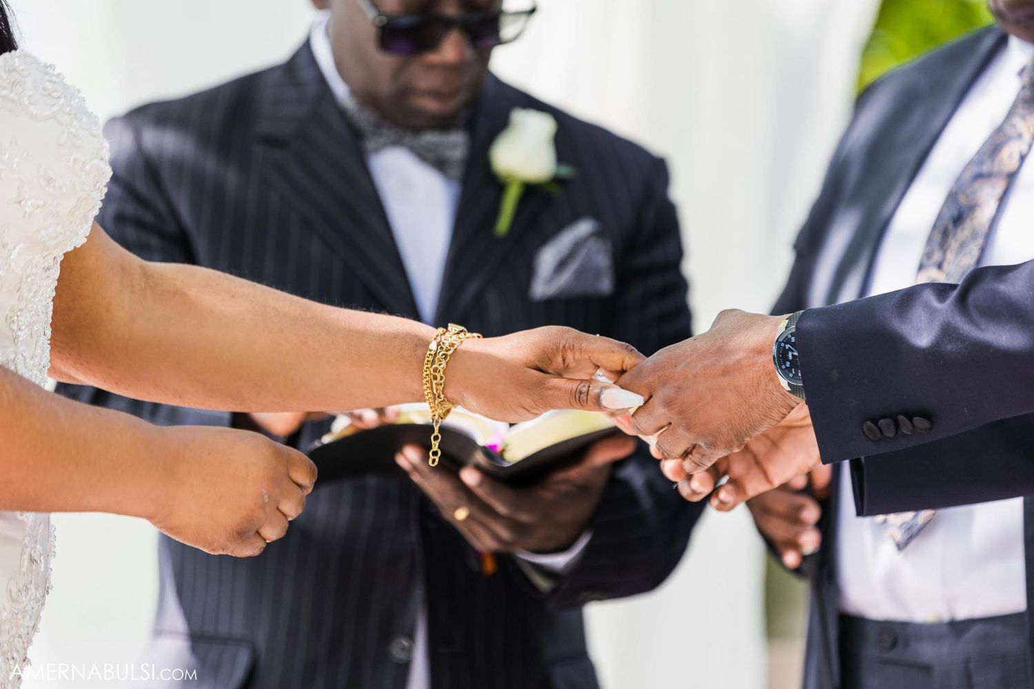 Close-up of hands during wedding ceremony ring exchange with officiant holding bible.
