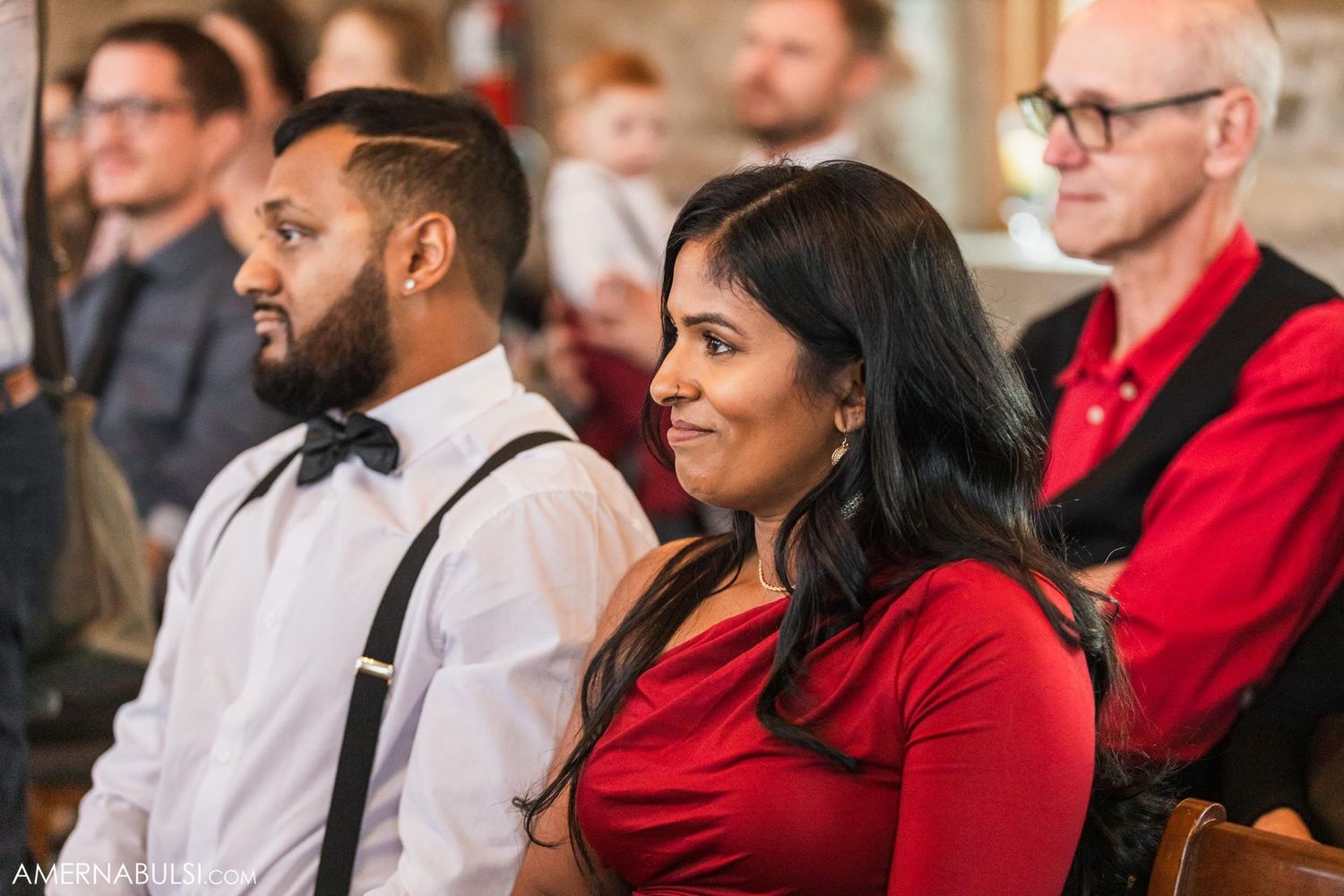 Wedding guests in formal attire seated and watching the ceremony indoors.