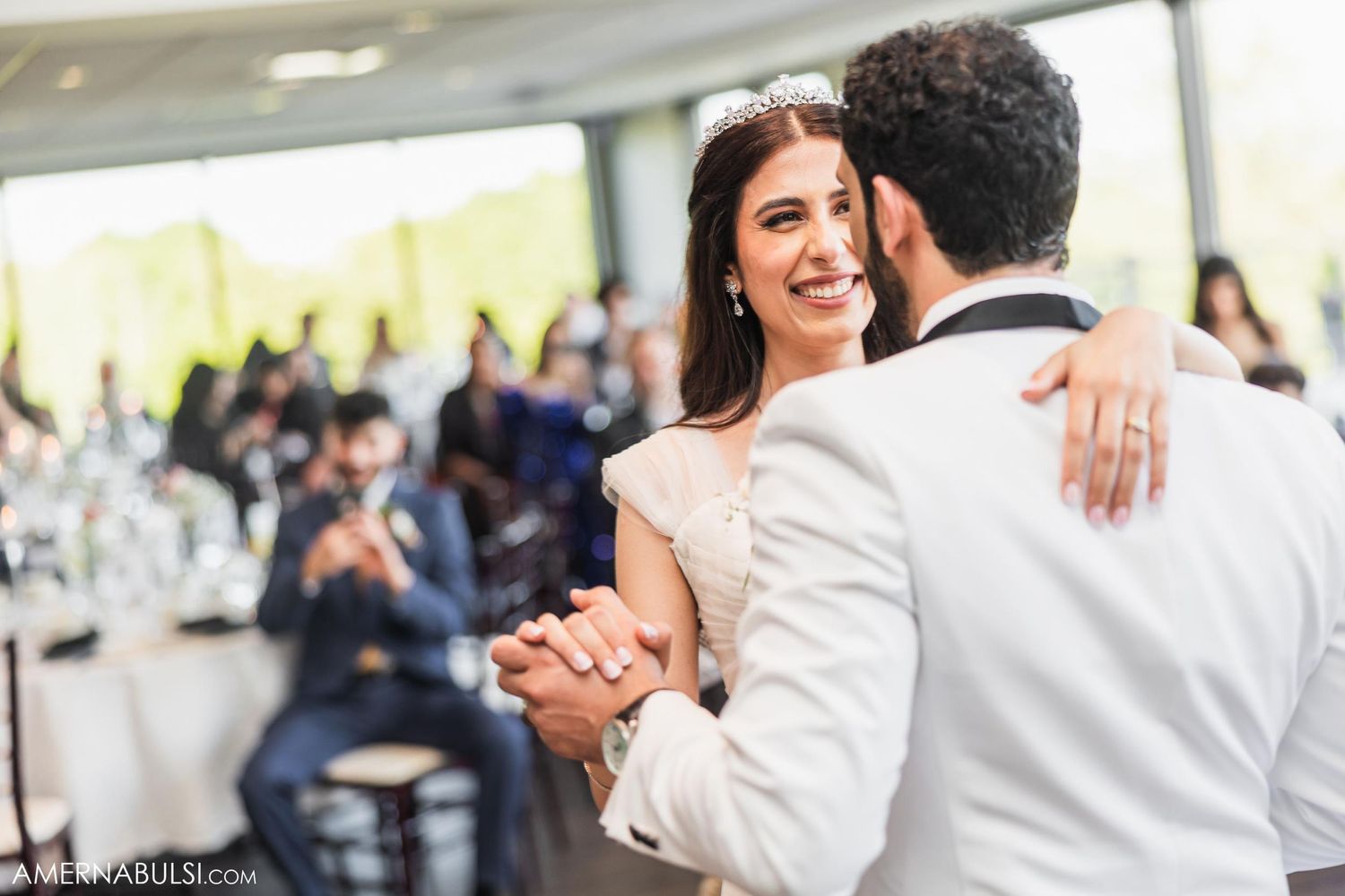 Couple shares their first dance at a wedding reception while guests watch and smile in the background.