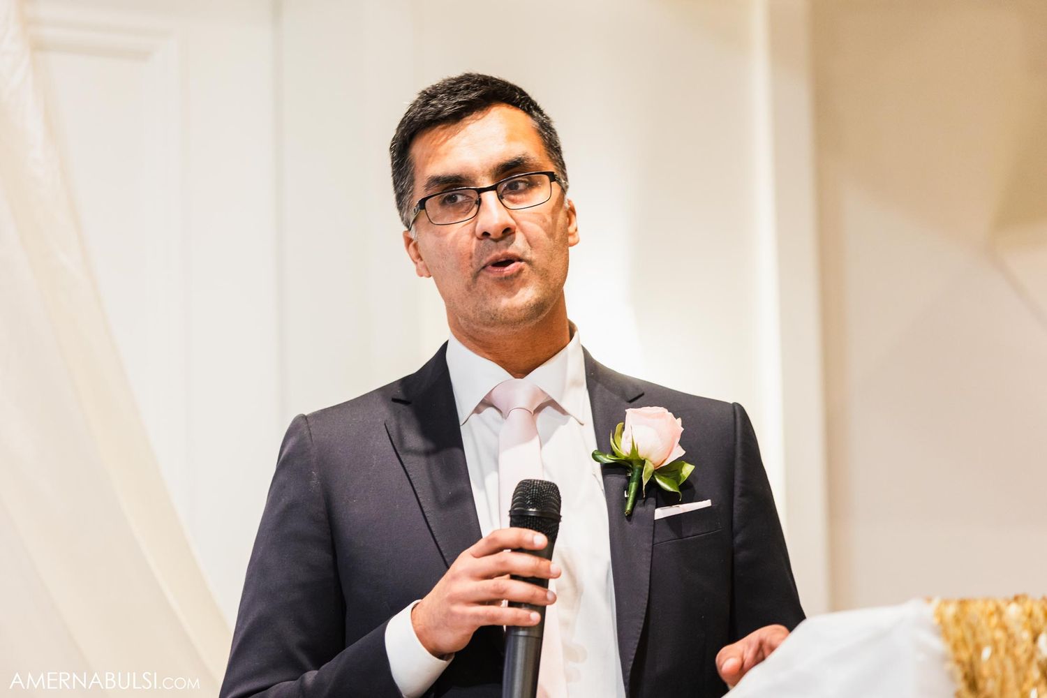 Wedding guest in formal attire gives a heartfelt speech with microphone during reception.