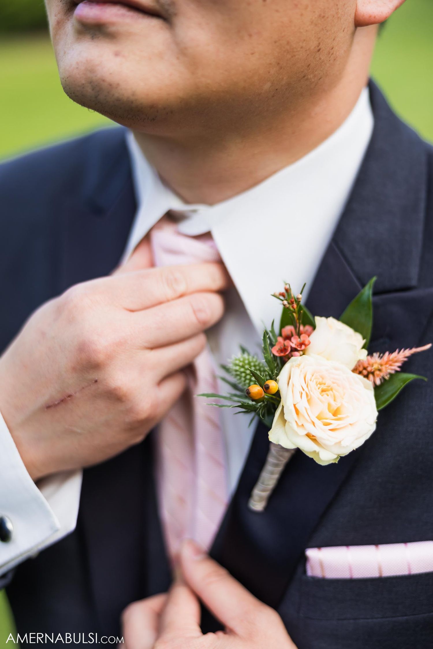 Close-up of peach rose boutonniere and pink tie on formal suit.