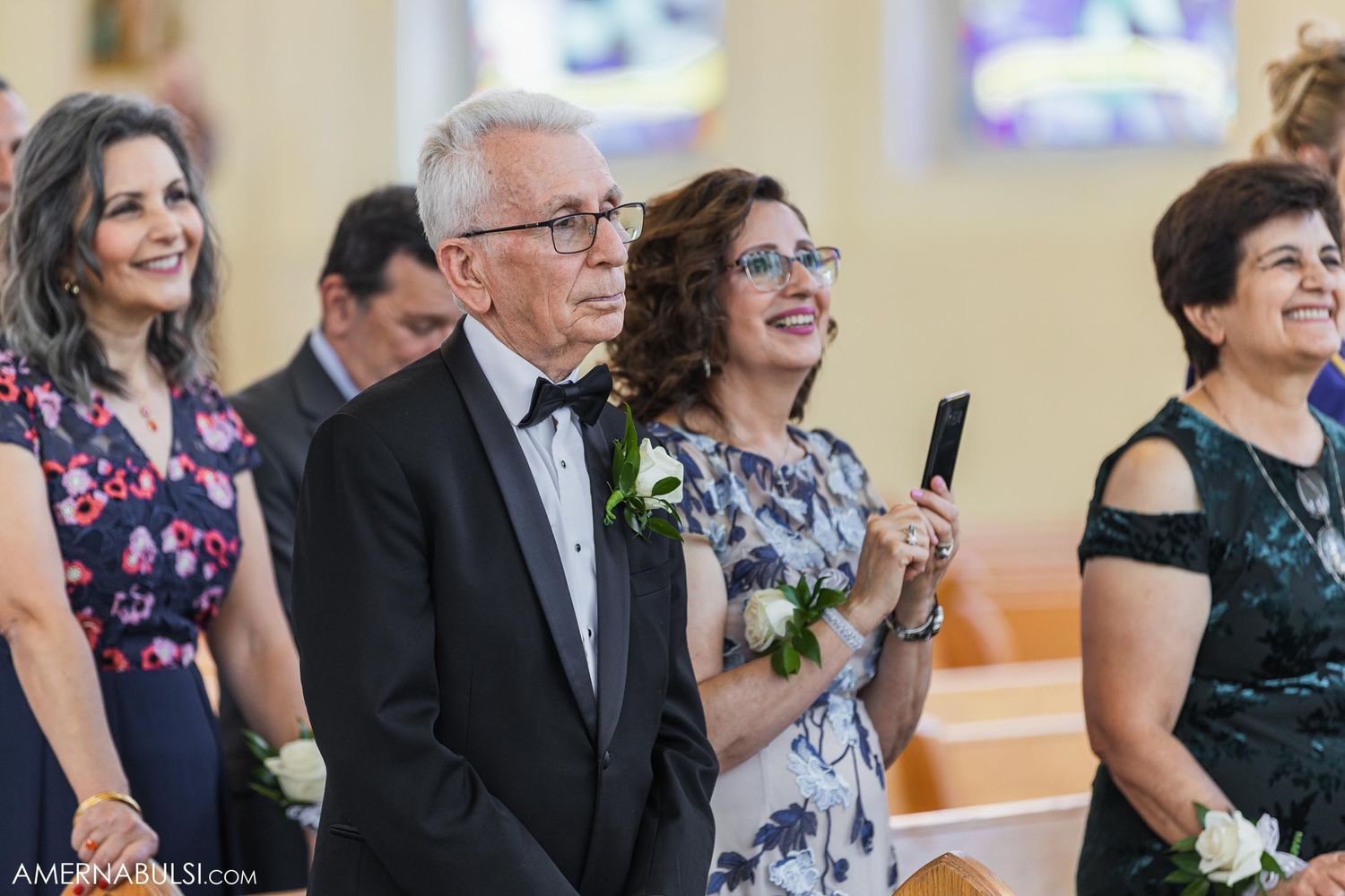 Wedding guests smile and watch the ceremony in formal attire.