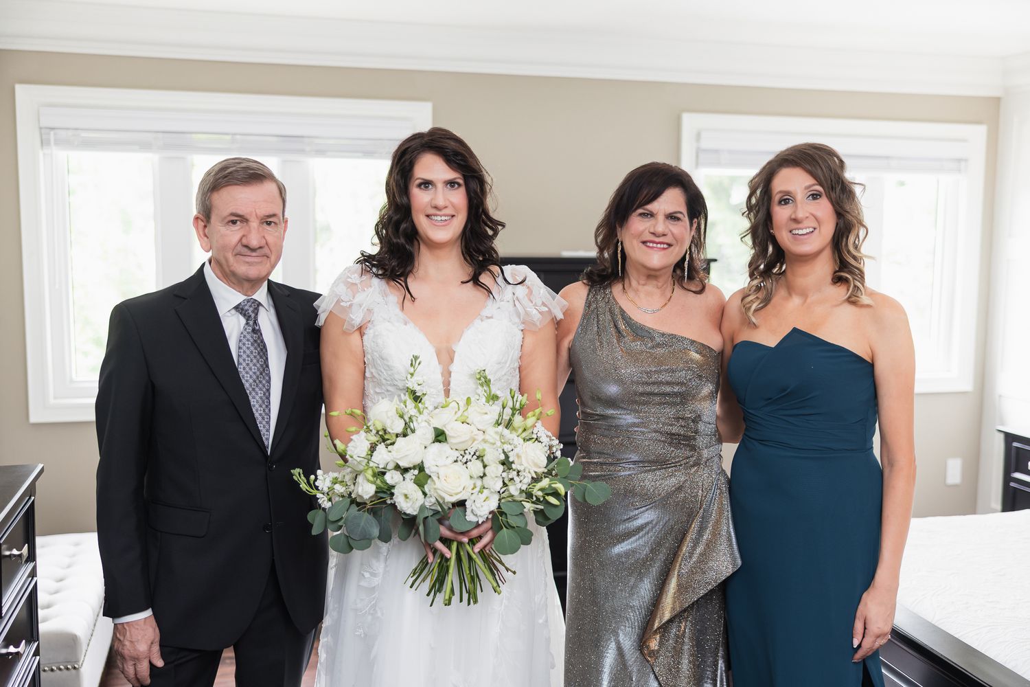 Bride with white bouquet poses with family members in formal attire before wedding ceremony.