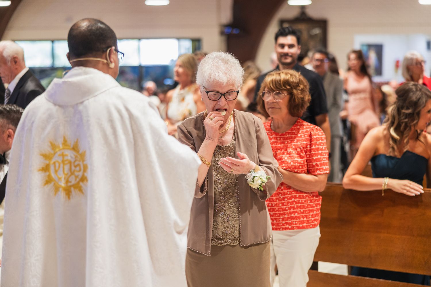 Elderly woman receiving communion from a priest during a Catholic church service with congregation in background.