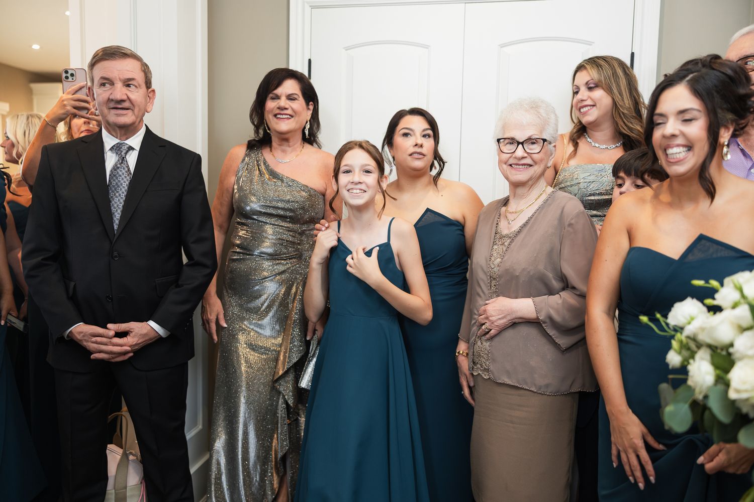 Wedding party group photo featuring bridesmaids in teal gowns with family members smiling indoors.