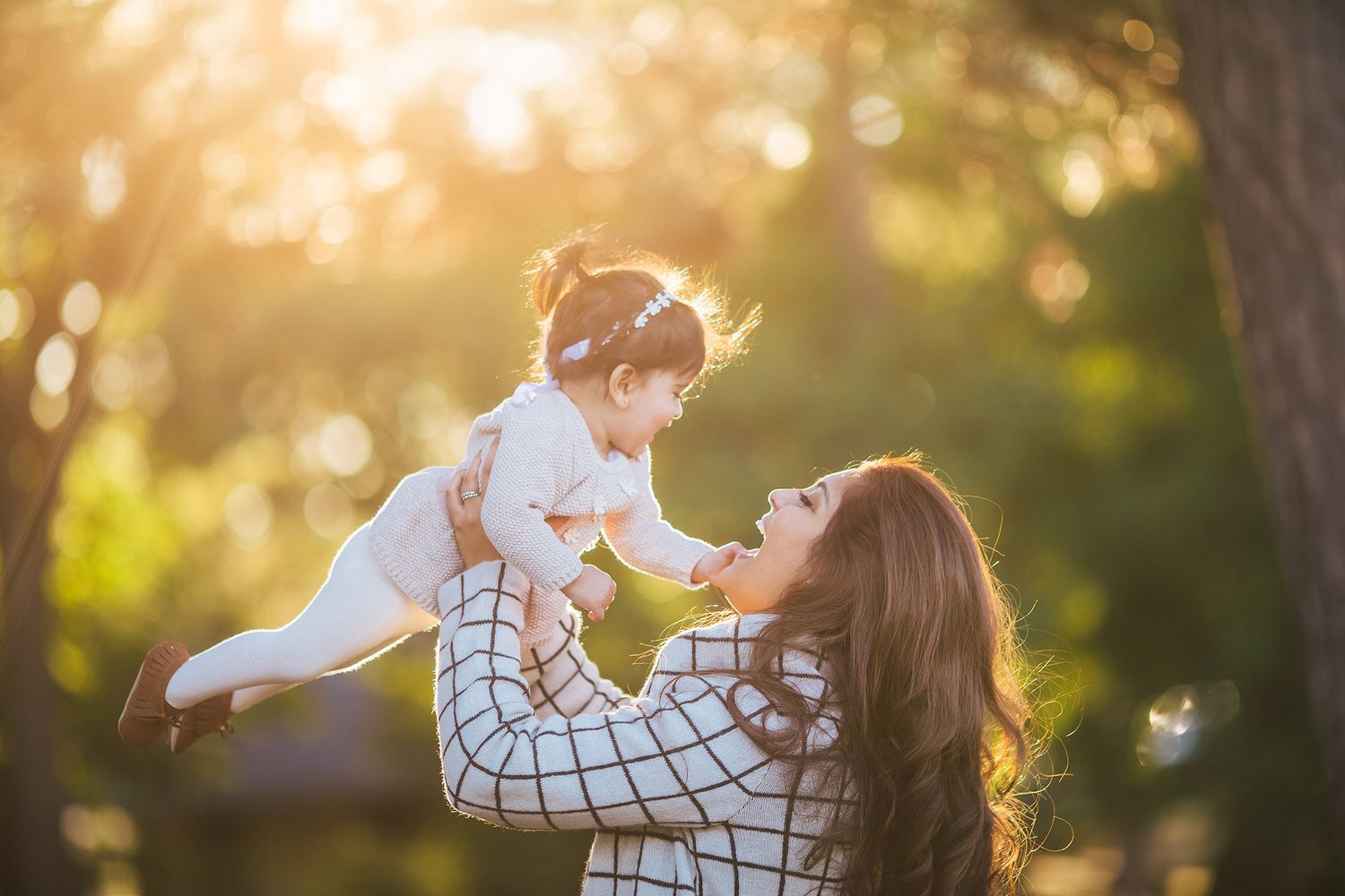 A parent lifts a small child in the air during golden hour, creating a joyful moment in nature with sunlit bokeh.