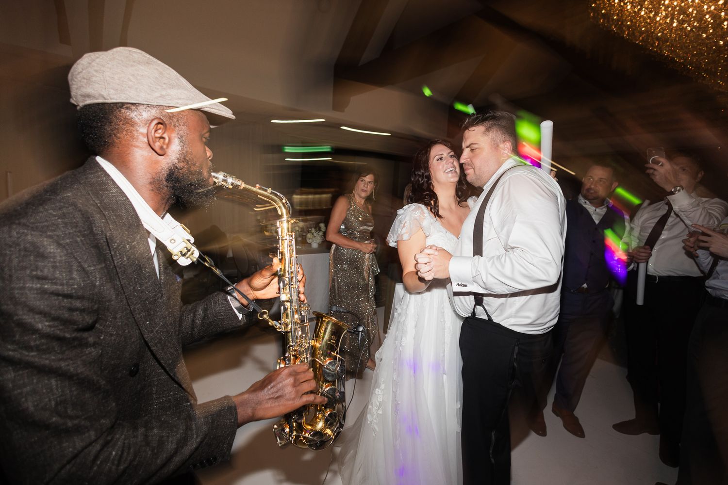 Saxophonist plays for bride and groom dancing at wedding reception with guests in background.