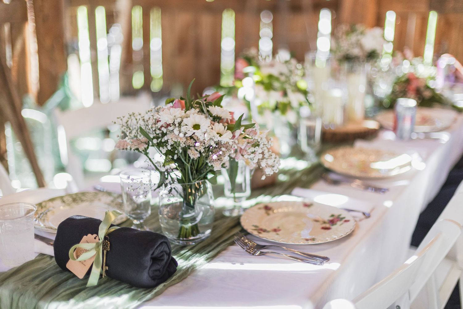 Elegant rustic wedding reception table set with floral centerpieces, folded napkins, and wooden charger plates.