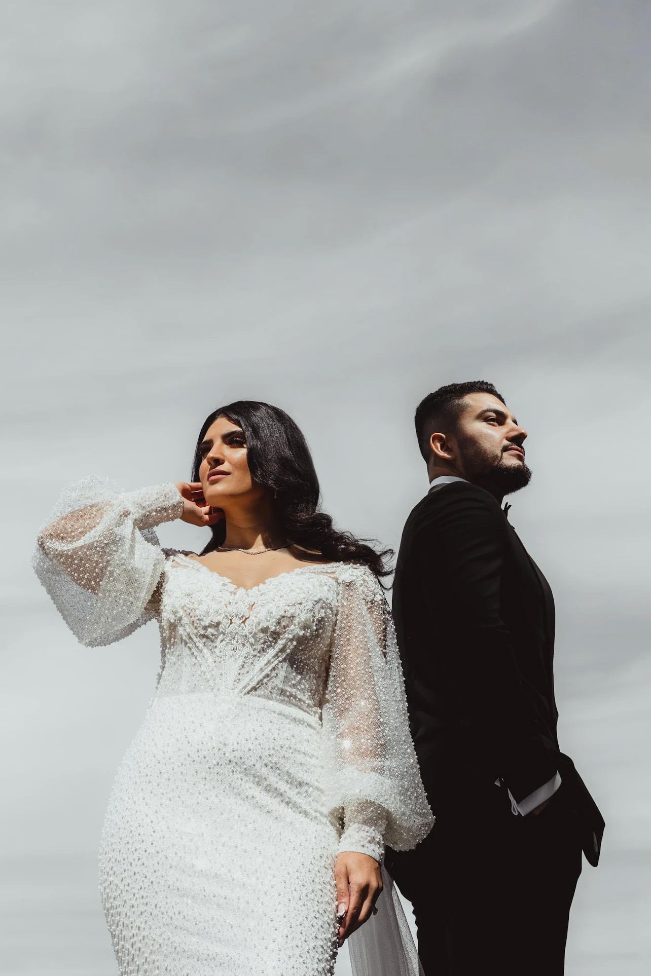 Artistic black and white wedding portrait with bride in lace dress posing dramatically against grey backdrop.