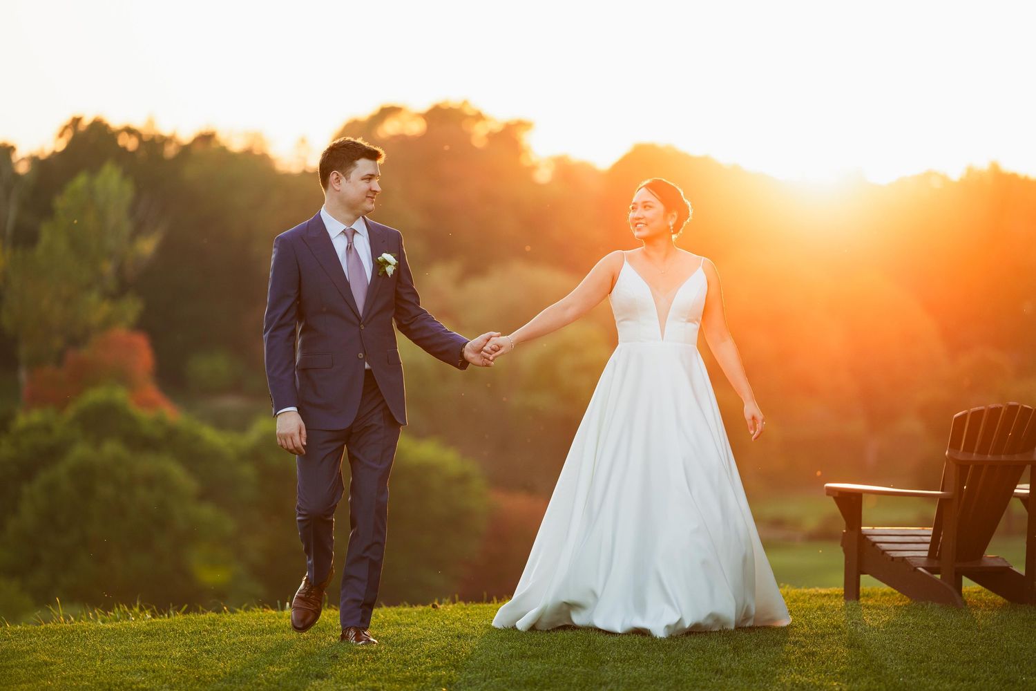 Wedding couple strolling through park during dramatic golden hour sunset.