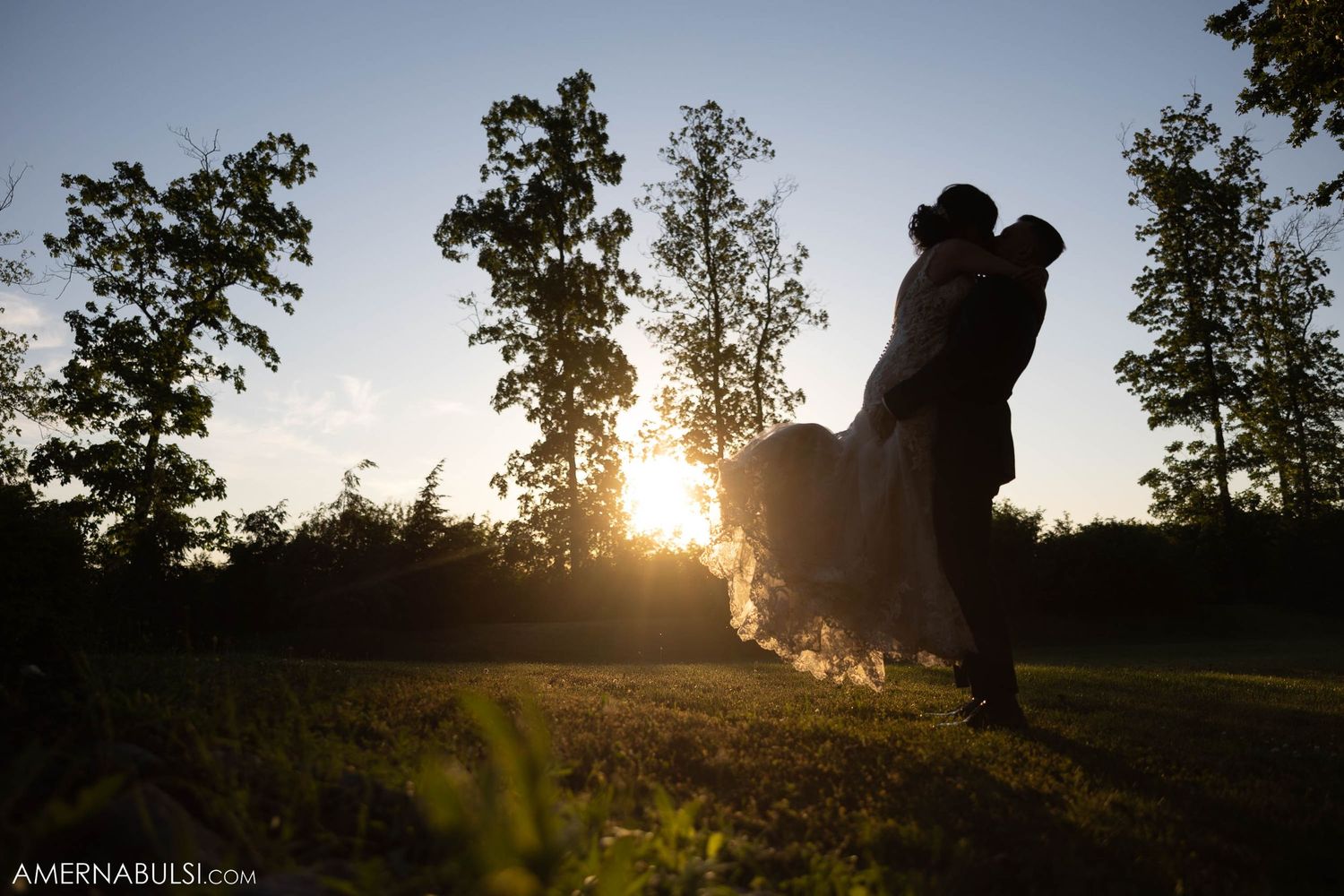 Silhouetted couple embracing at sunset with trees in the background.