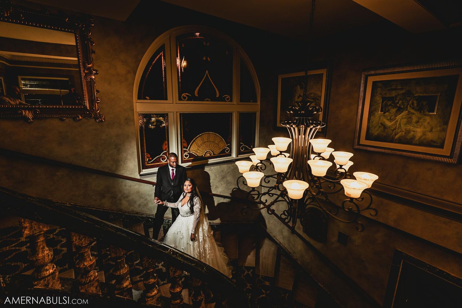 Elegant wedding venue interior showing a spiral staircase and chandelier with couple descending.