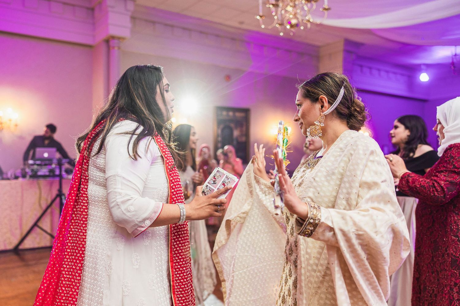 Wedding guests in elegant traditional South Asian attire socializing at a purple-lit reception.