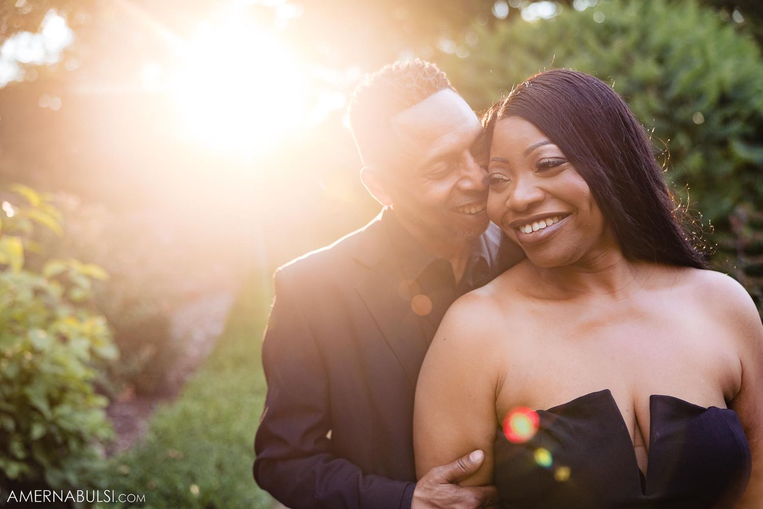 Couple shares joyful moment in garden with warm sunset glow and lens flare.