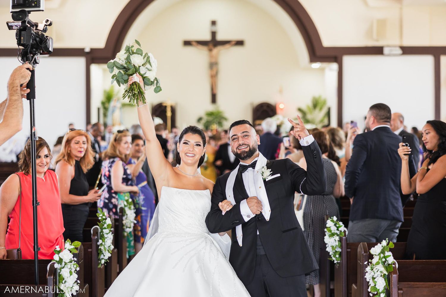 Newlyweds celebrate joyfully during recessional while wedding guests take photos in church.