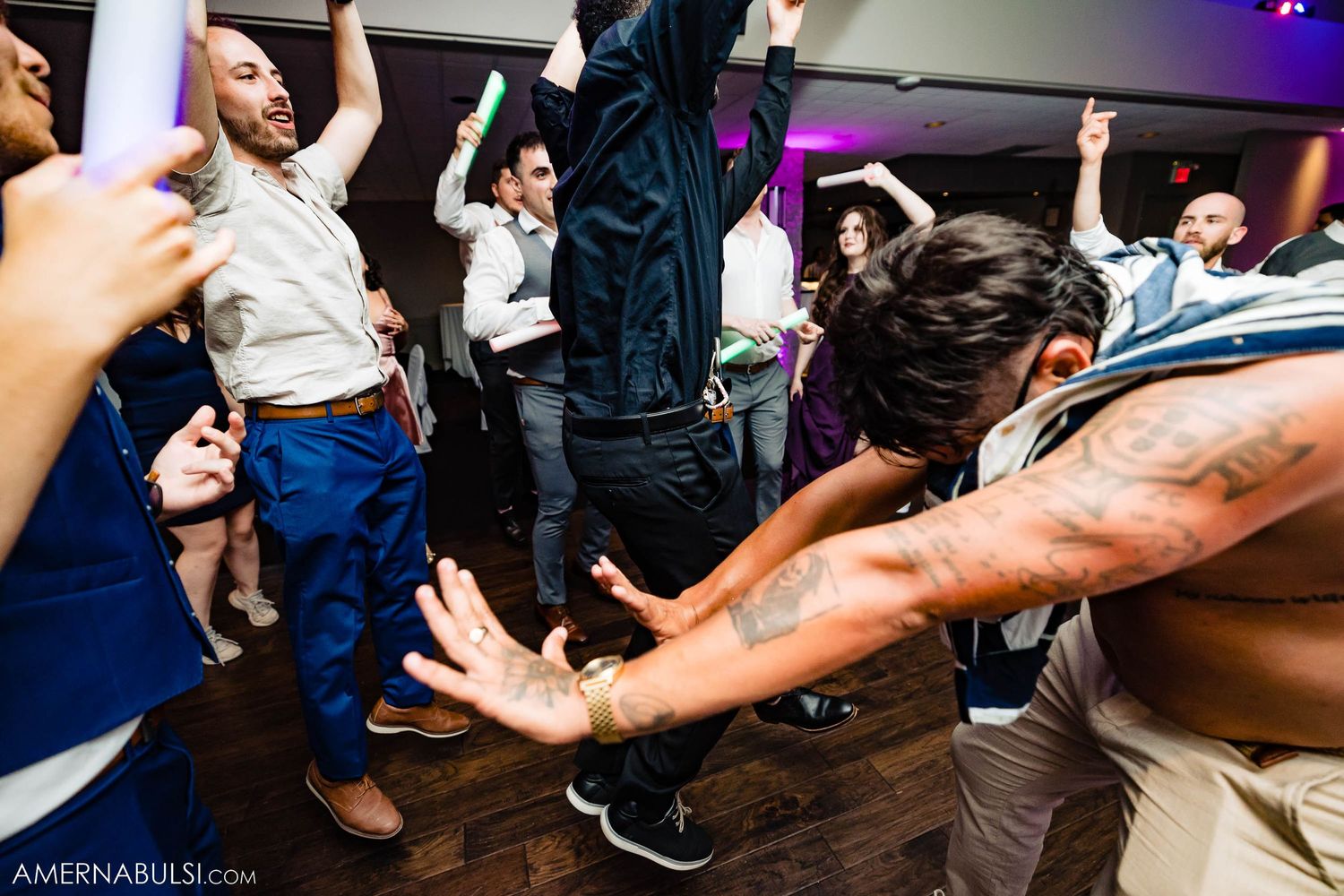 Wedding party guests dancing energetically with arms raised on wooden dance floor.