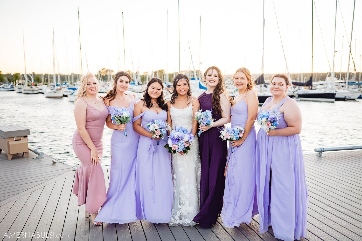 Bridal party in lavender and pink dresses posing by marina with boats.
