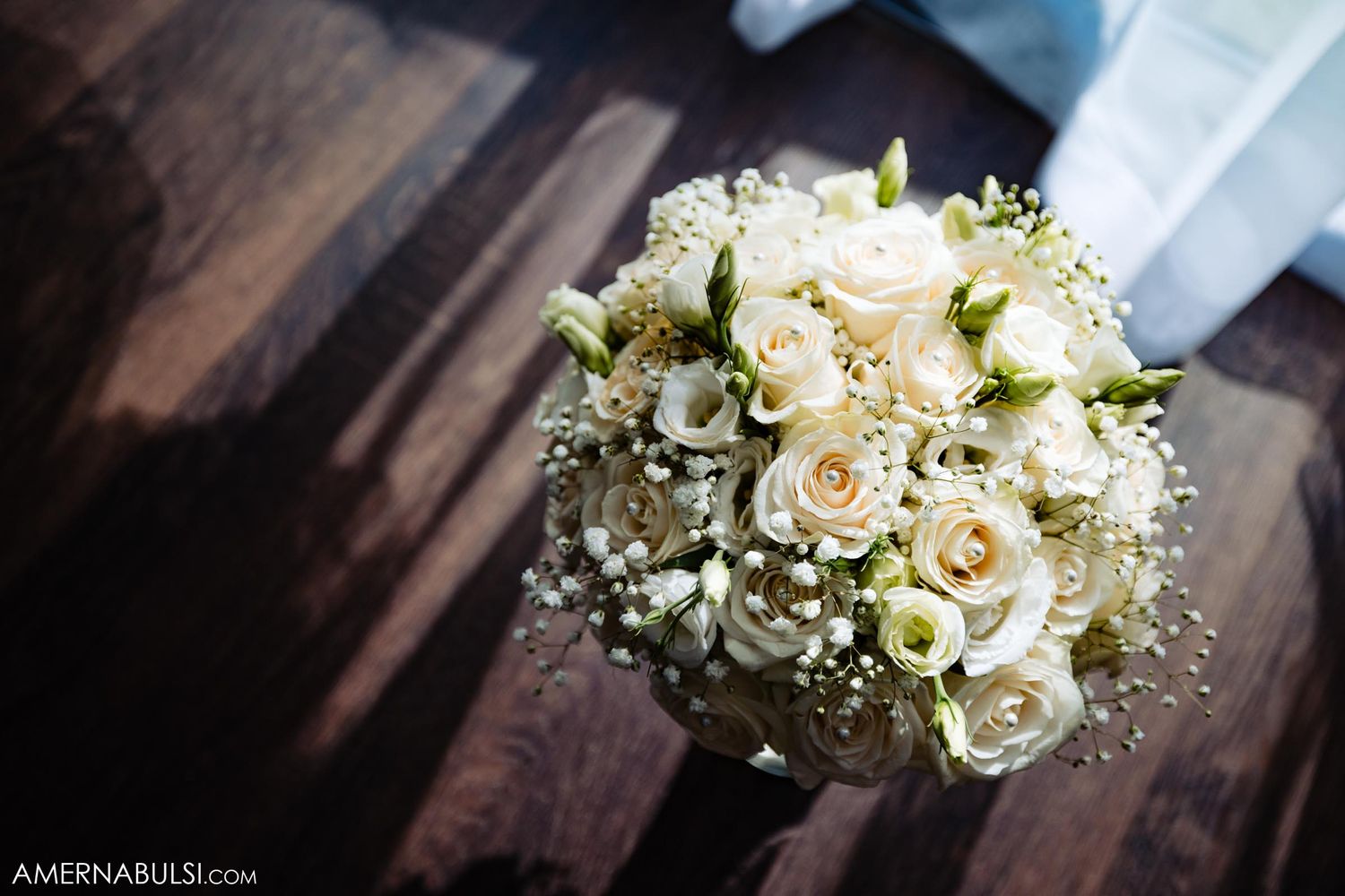 Elegant white rose and baby's breath wedding bouquet on dark wooden surface.