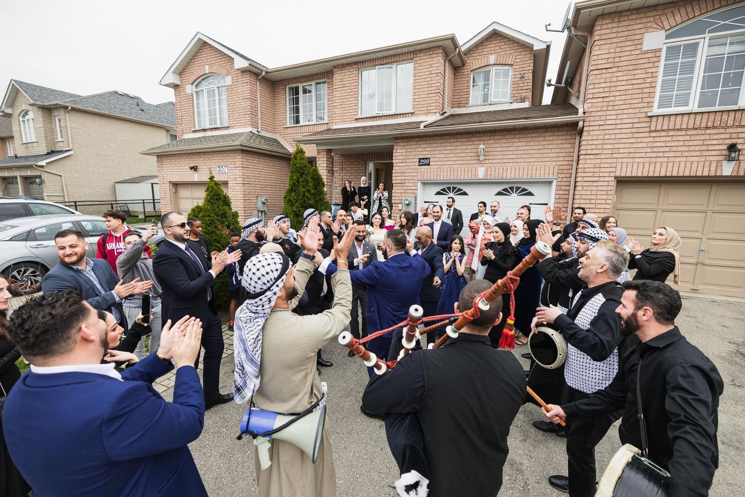 Crowd of wedding guests celebrating outdoors in front of suburban homes.