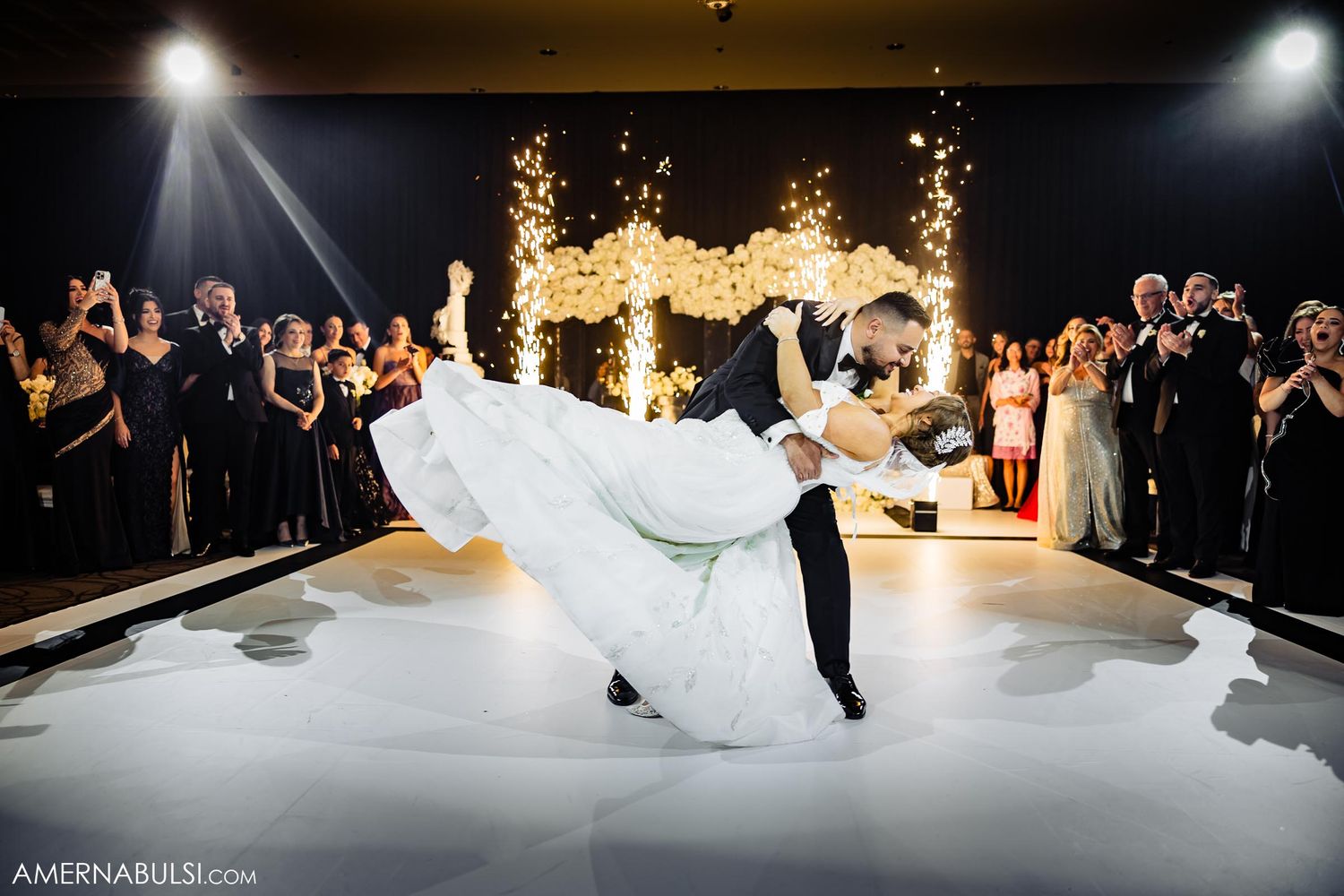Newlyweds perform an elegant dip during their first dance surrounded by sparklers and wedding guests.