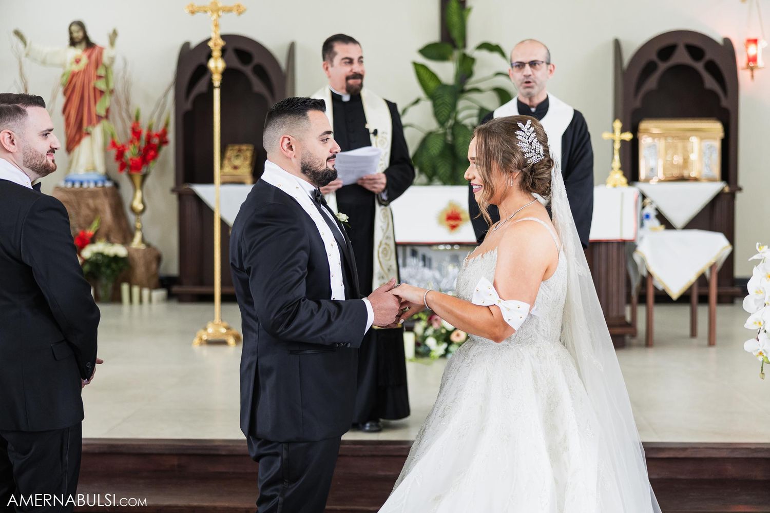 Wedding ceremony in progress inside traditional Catholic church with religious statues and altar.