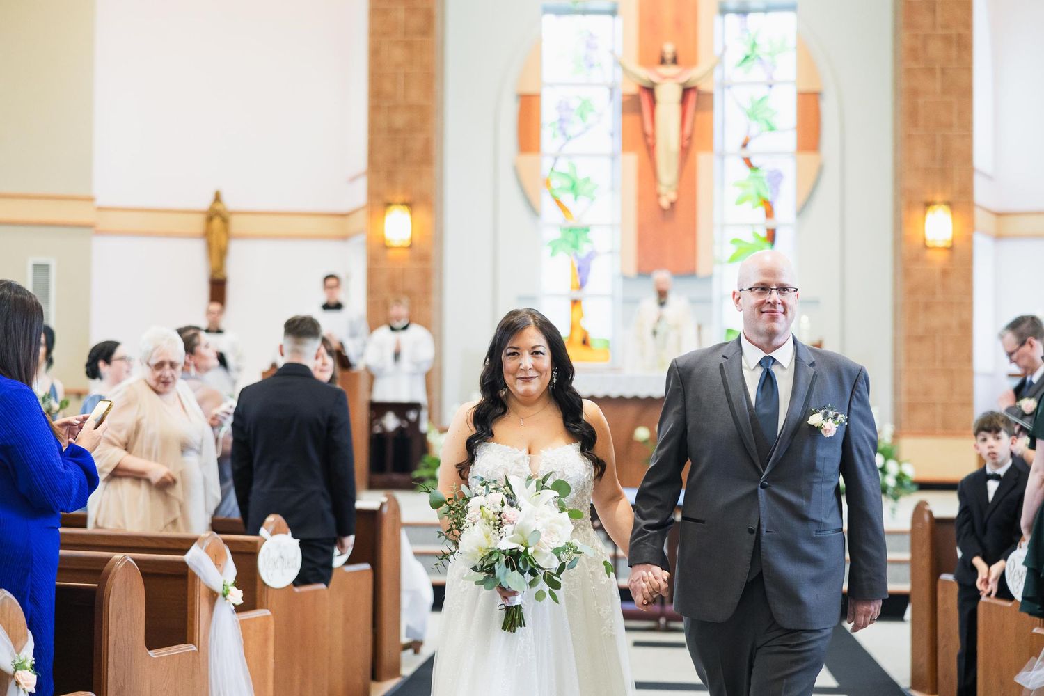 Couple walks down church aisle after ceremony with guests looking on.