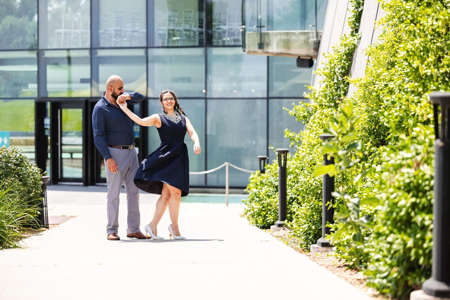 A couple takes a stroll together on a sunny path near a modern glass building.