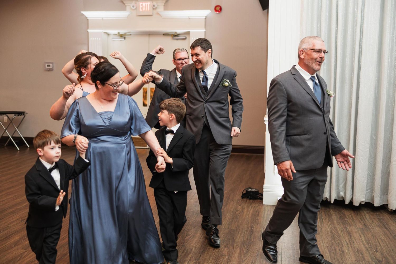 Guests dancing enthusiastically at a wedding reception on a wooden dance floor.