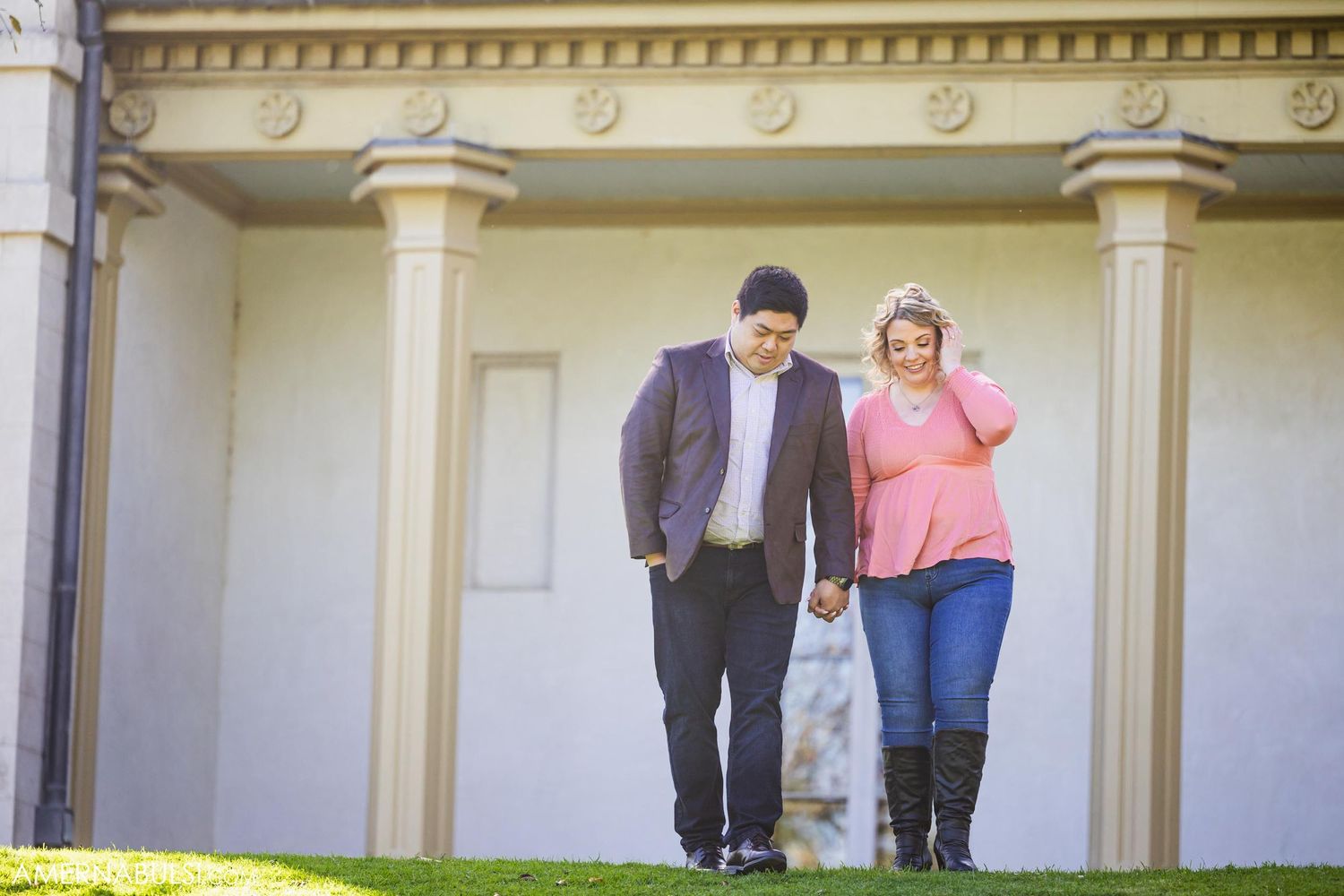 A couple walks together along the front of a historic building with columns and ornate architecture.