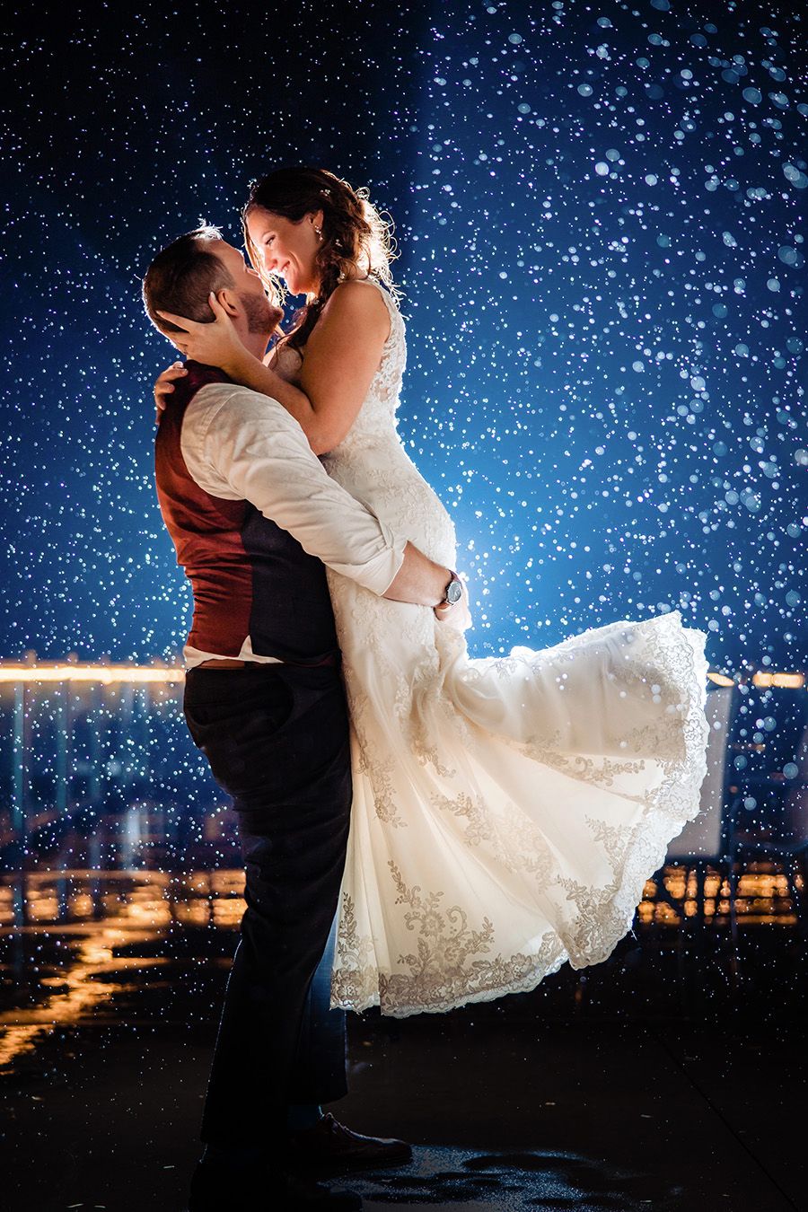Magical nighttime wedding dance photos with sparkling snow and city lights in the background.